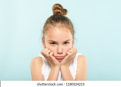 Emotion Face. Frowning Grumpy Child With Pursed Lips And Sad Look. Young Cute Girl Portrait On Blue Background.