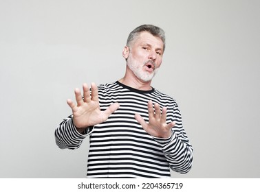 Emotion, Lifestyle And Old People Concept: Portrait Senior Bearded Man, Looking Shocked, Scared Trying To Protect Himself In Anticipation Of Unpleasant Situation, Isolated On Grey Background.