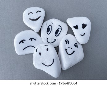 Emotion management concept, stones with painted faces symbolize different emotions. We are all different, but all together, learning to manage emotions. White stones on grey background. - Shutterstock ID 1936498084
