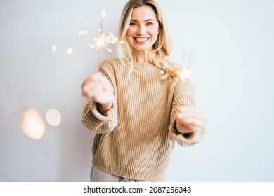 Emotion portrait of young blond woman in knitted cozy sweater with holding burning sparklers at white background. People, holidays, celebrating, party, emotion and glamour concept.