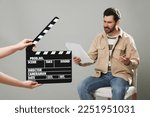 Emotional actor performing while second assistant camera holding clapperboard on grey background, closeup
