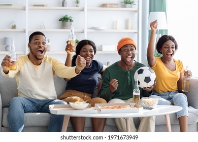 Emotional African American Friends Drinking Beer And Eating Snacks, Watching Football Game On TV At Home Together. Cheerful Black Men And Women Fans Watching Sport Match, Gesturing And Screaming