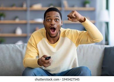 Emotional African American Man Having Fun At Home, Screaming With Remote Controller In His Hand, Watching Football Game On TV, Empty Space. Black Guy Enjoying His Weekend, Watching TV In Living Room