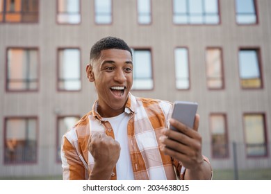 Emotional African American Man Using Mobile Phone, Shopping Online On The Street. Happy Guy Celebration Success, Sports Betting Concept	
