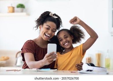 Emotional African American Mother And Daughter Sitting At Kitchen Table Taking Selfie Together While Spending Time Together, Happy Black Mom And Kid Having Video Chat, Using Cellphone, Copy Space