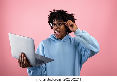 Emotional African American Teen Looking At Laptop Screen, Opening Mouth In Shock, Excited About Win Or Success On Pink Background. Black Teenage Guy With Portable Pc Cannot Believe Huge Online Sale