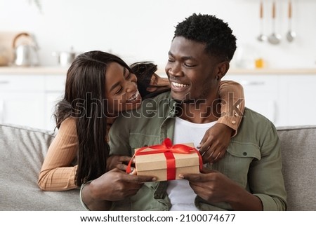 Emotional african american woman hugging lover, giving gift box, making great surprise for St. Valentines Day, home interior, free space. Happy black lady embracing her husband, holding present