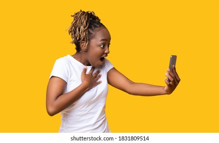 Emotional African American Young Woman With Open Mouth Looking At Mobile Phone, Yellow Studio Background, Panorama With Copy Space. Excited African American Lady Holding Smartphone, Side View