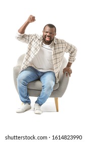 Emotional African-American Man Watching TV While Sitting In Armchair Against White Background