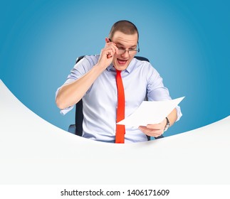 Emotional And Ambitious Young Leader Sits At The Table And Works With Documents And Papers. On A Blue Background Studio Photography