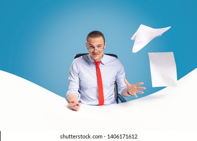 Emotional And Ambitious Young Leader Sits At The Table And Works With Documents And Papers. On A Blue Background Studio Photography