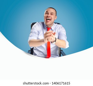 Emotional And Ambitious Young Leader Sits At The Table And Works With Documents And Papers. On A Blue Background Studio Photography