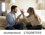 Emotional annoyed stressed couple sitting on couch, arguing at home. Angry irritated nervous woman man shouting at each other, figuring out relations, feeling outraged, relationship problems concept.