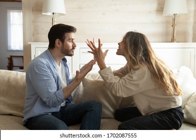 Emotional annoyed stressed couple sitting on couch, arguing at home. Angry irritated nervous woman man shouting at each other, figuring out relations, feeling outraged, relationship problems concept.
