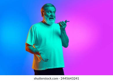 Emotional bearded senior man recording voice message via mobile phone on gradient blue-purple background in neon light. Concept of human emotions, lifestyle, casual fashion - Powered by Shutterstock