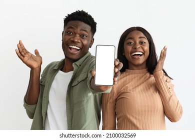 Emotional Beautiful African American Young Couple Showing Newest Cellphone With Empty Screen, Smiling And Gesturing, Enjoying Nice Mobile Application, White Studio Background, Mockup