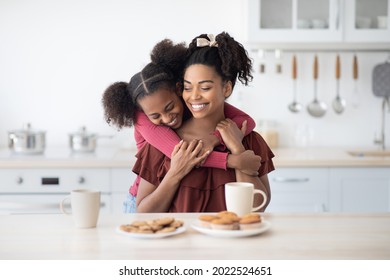 Emotional black daughter teenager hugging her beautiful happy mom while enjoying cookies, homemade pastry and biscuits together at home, kitchen interior. Family lifestyle, motherhood, parenthood