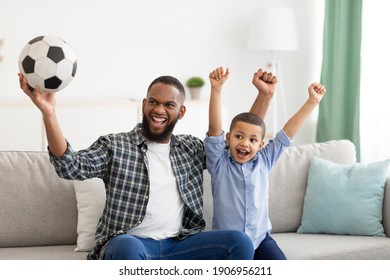 Emotional Black Father And Son Watching Sports On Television Shaking Fists Celebrating Victory Of Favorite Soccer Team At Home. Family Leisure And Entertainment. Sport TV Programming