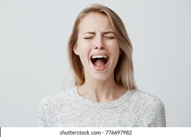 Emotional blonde woman opening her mouth widely screaming loudly being dissatisfied with something expressing disagreement and annoyance. Female shouting at boyfriend, Negative emotions and feelings