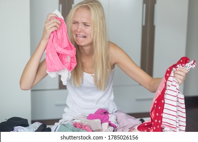 Emotional Breakdown. Crying Young Woman Sorting Through A Pile Of Laundry Clothes From Her Closet. Household Chores And Clutter.