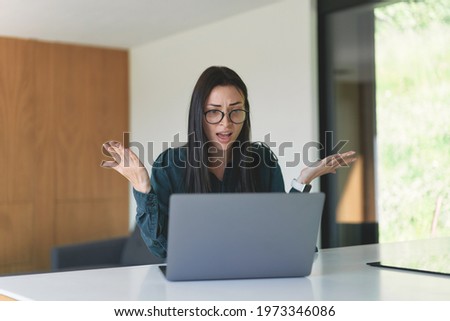 Emotional business woman working from home with laptop. Young woman in glasses discussing financial problem online throws up hands to the side don't understand while sitting at the table