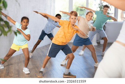 Emotional cheerful tween boy enjoying contemporary dance with group of children, showcasing dabbing move..