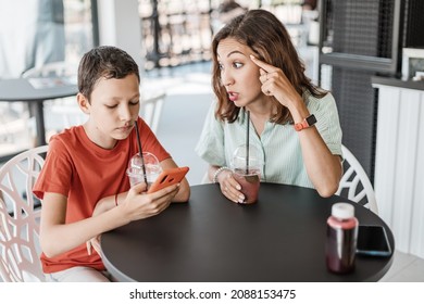 Emotional Conflict Between Mother And Son About Smartphone Addiction In Cafe. An Angry Mom And A Teenager Ignoring Her.