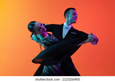 Emotional dancing couple  beautiful man   woman dancing waltz isolated over gradient orange pink background in neon light  Concept art  beauty  grace  action  emotions  Look delighted