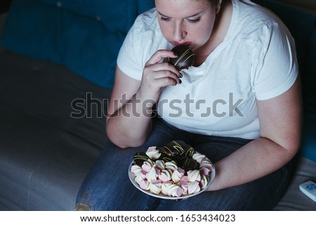Emotional eating, mental disorder, depression, loneliness, stress. Lonely woman eating sweets and watching tv late in the night. Nerve food