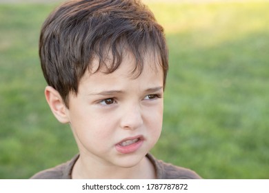 Emotional Face Of A Child. Close Up. Scared, Insecure Kid. Looking Away. The Mouth Is Crooked. Green Grass On The Background. Horizontal. Copy Space.