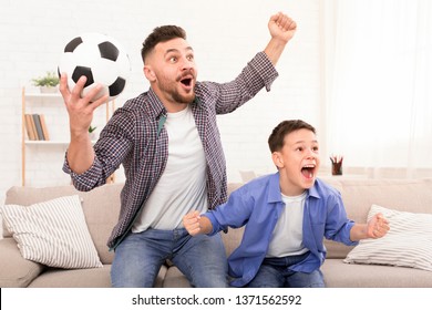 Emotional Father And Son Soccer Fans Cheering With Football Ball, Watching Sport On Tv At Home