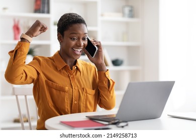 Emotional Female Entrepreneur Millennial Short-haired African American Lady Working Online From Office, Talking On Cell Phone, Looking At Laptop Screen And Gesturing, Successful Business Deal