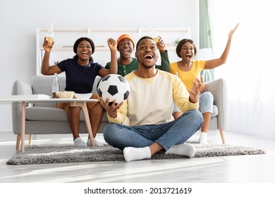 Emotional football fans young african american men and women watching game together at home, celebrating win of their team, raising hands up and screaming, excited black guy with soccer ball - Shutterstock ID 2013721619