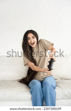 Emotional girl playing online video game console sitting on couch in front of tv in modern minimal living room vertical