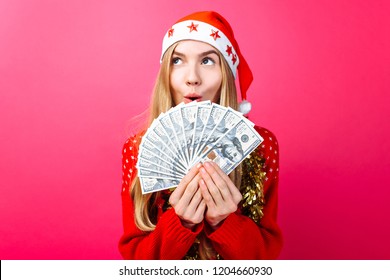 Emotional girl in a red sweater and Santa Claus hat, in admiration holding money on a red background. Christmas, business