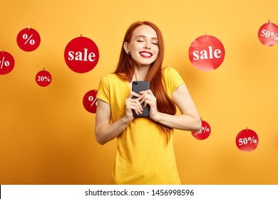emotional girl rejoicing at her new mobile phone which she has bought during the sale. close up portrait. happiness, pleasure concept. dreams come true. isolated yellow background