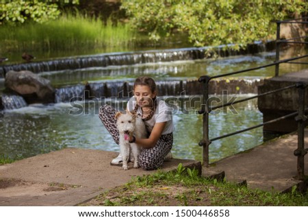 Emotional girl teenager with long hair hairstyle braids in a green shirt reared dog fox terrier in the park.