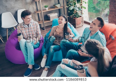 Emotional and glad youngsters sit in multi-colored armchairs with drinks in hands and loud laugh at the funny stories and comic jokes classmates sit in chair bag