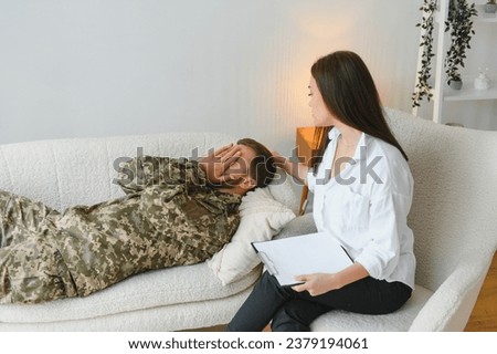 Emotional guy in camouflage uniform laying on couch, gesturing while having conversation with psychotherapist at clinic, soldier suffering from posttraumatic stress disorder
