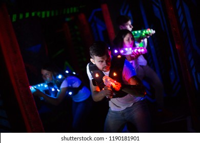 Emotional guy with laser pistol playing laser tag with friends on dark labyrinth