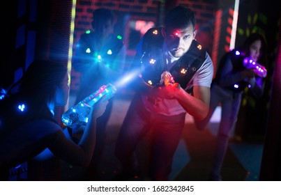 Emotional guy playing laser tag with friends on dark labyrinth in colorful beams of laser pistols 