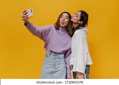 Emotional Happy Girls Have Fun And Demonstrate Tongues. Pretty Young Asian Women Take Selfie And Make Funny Faces On Orange Background.