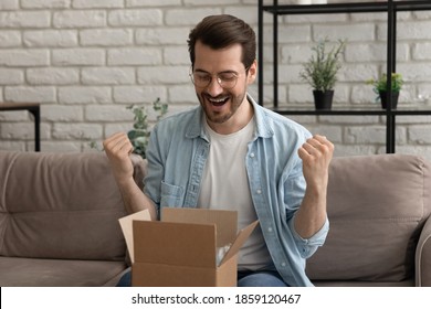 Emotional Happy Young Man In Eyeglasses Opening Small Cardboard Parcel, Celebrating Getting Wished Item, Satisfied With Shopping Experience In Online Store Or Fast Delivery Service, Getting Gift.