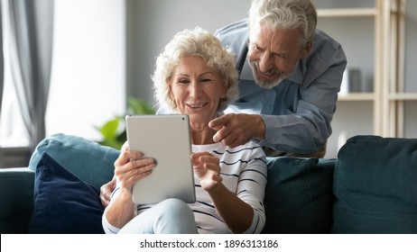 Emotional Joyful Middle Aged Senior Family Couple Watching Funny Photos Or Videos Online On Digital Computer Tablet, Having Fun Web Surfing Information Or Enjoying Shopping In Internet Store.