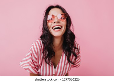 Emotional latin girl in sparkle sunglasses laughing to camera. Adorable female model enjoying photoshoot in pink clothes