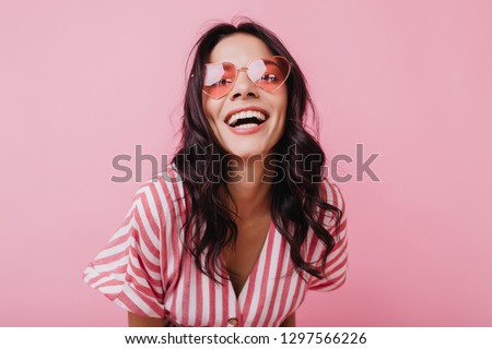 Emotional latin girl in sparkle sunglasses laughing to camera. Adorable female model enjoying photoshoot in pink clothes
