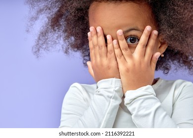 emotional little black girl covers face with hand isolated over purple background, child watching horror film, movie, reaction, facial expression. children and human emotions concept