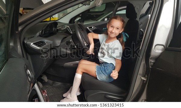 emotional little girl in the car behind the wheel.\
She wears blue shorts and sneakers. Child smiles kindly. Concept of\
model kid, car fashion, fun.\
