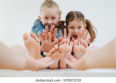 Emotional little siblings sitting on a table with bare feet. Hands reaching them to tickle. Making stop gesture. Faces blurred, focus on their feet.