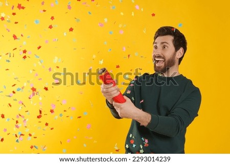Emotional man blowing up party popper on yellow background